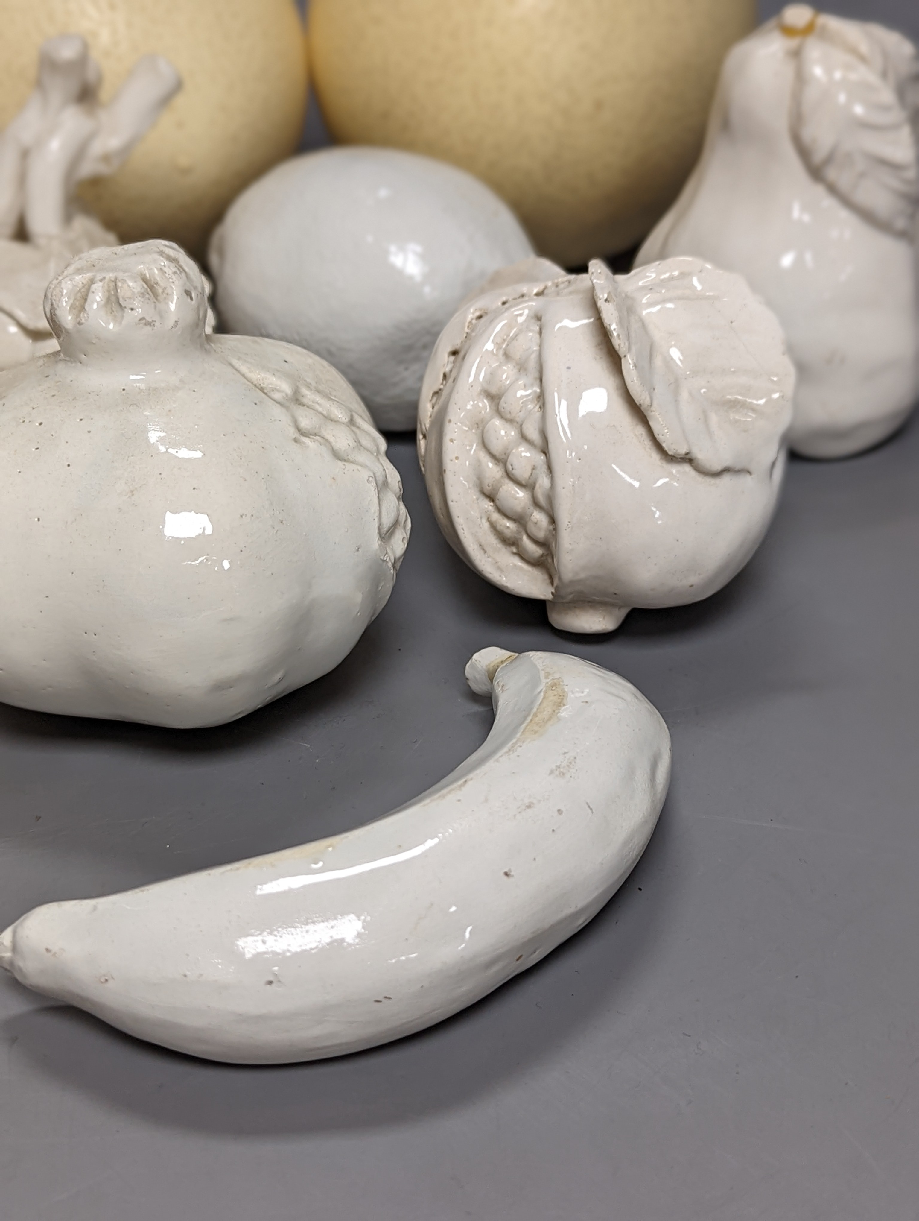 A decorative collection of tin glazed model fruits, together with three ostrich eggs